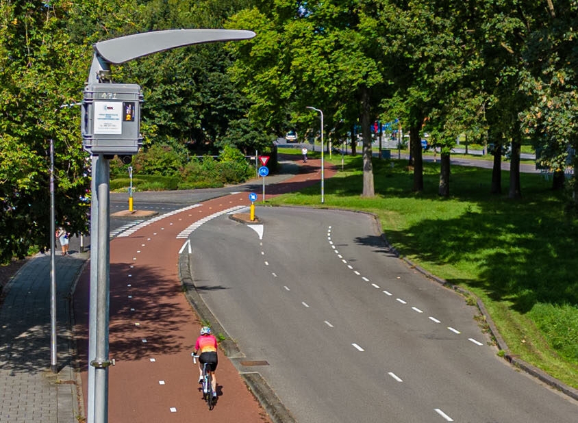 Geautomatiseerde vorm van verkeerstelling boven een weg in de bebouwde kom met zijdelings een dubbel fietspad in een groene omgeving. 